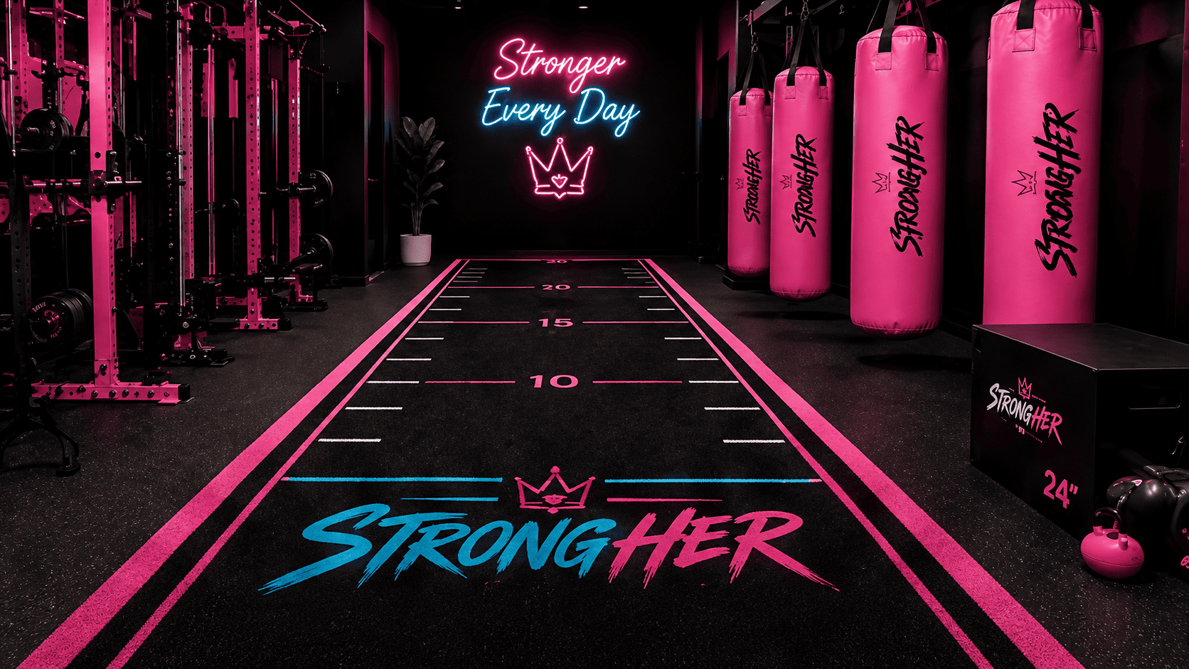 Dark training floor with pink StrongHer heavy bags and neon signage